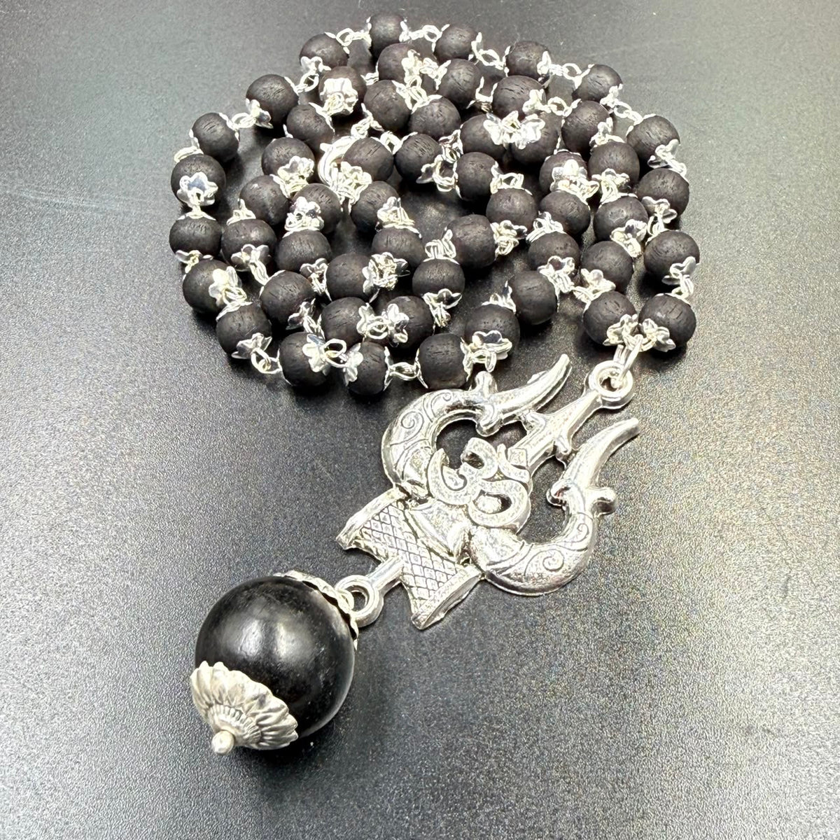 Karungali bead mala with Om Trishul metal pendant laid on grey background with bead links