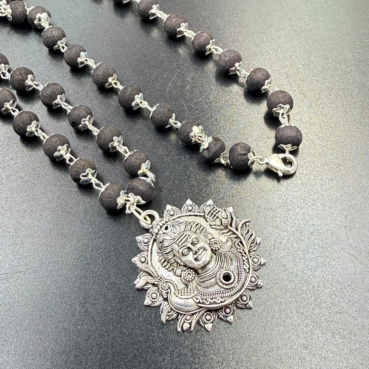 Karungali bead mala string necklace with Lord Shiva face metal pendant on tabletop