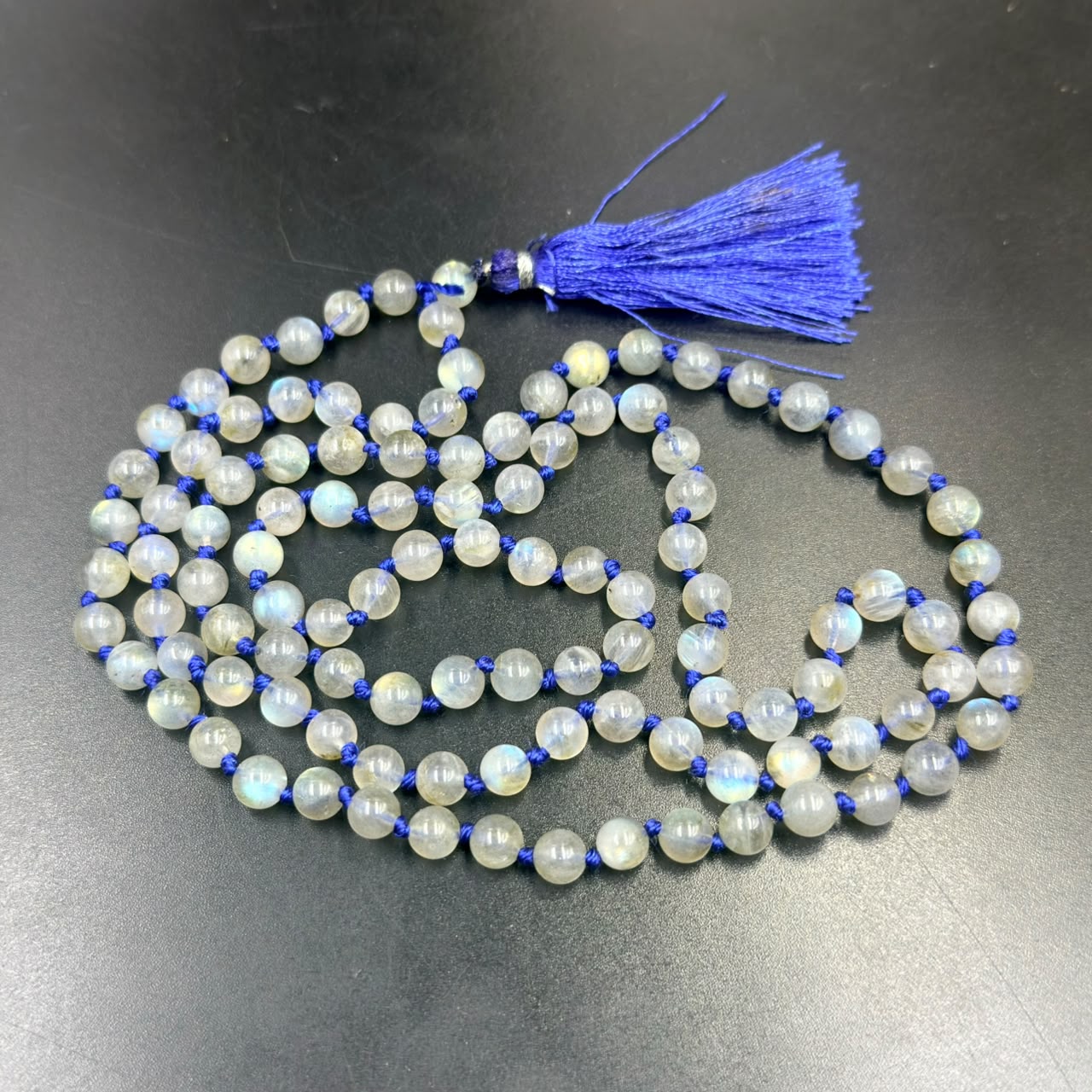 Labradorite mala beads with blue tassel shown laid on a dark surface