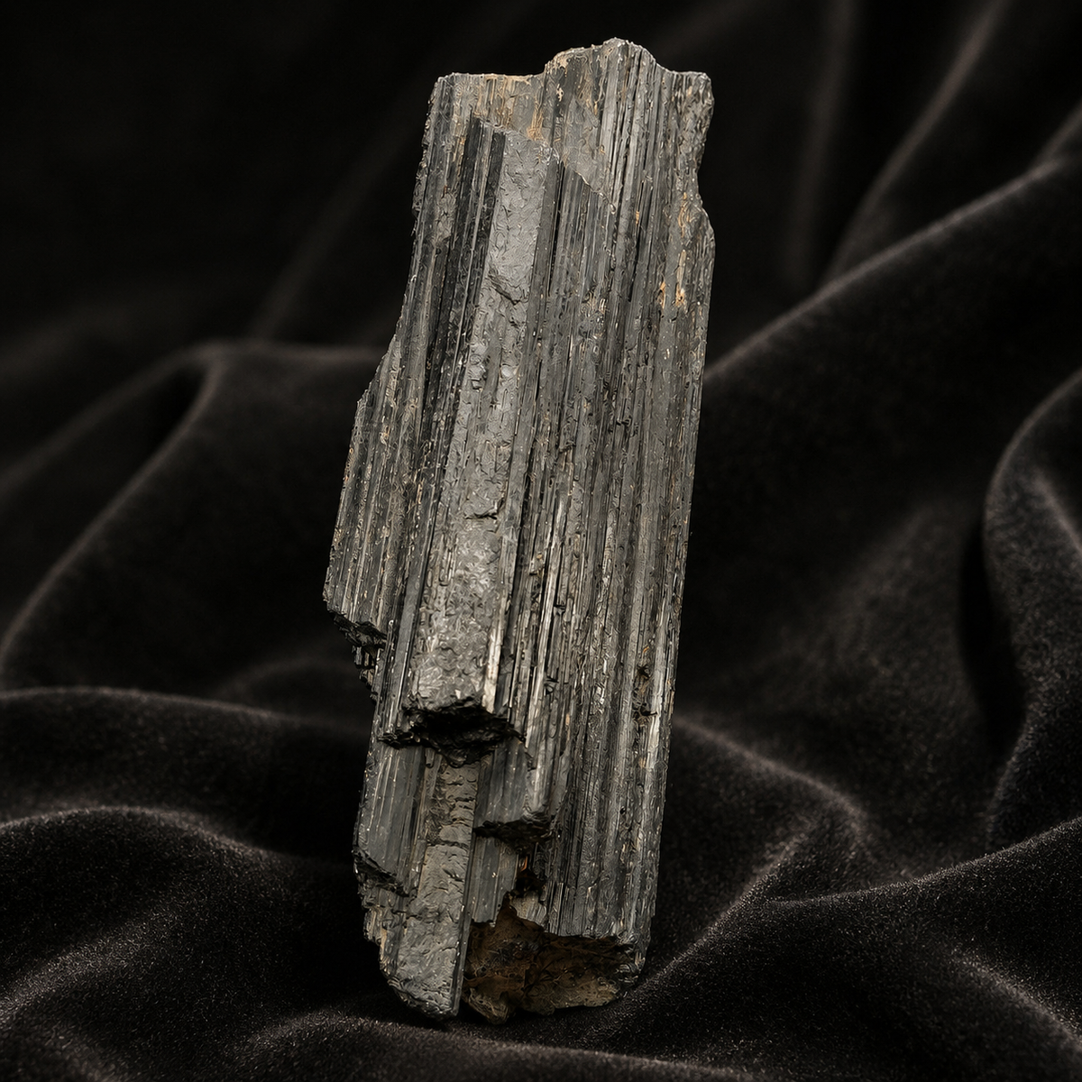 Large rough black tourmaline crystal with vertical banded striations on dark fabric