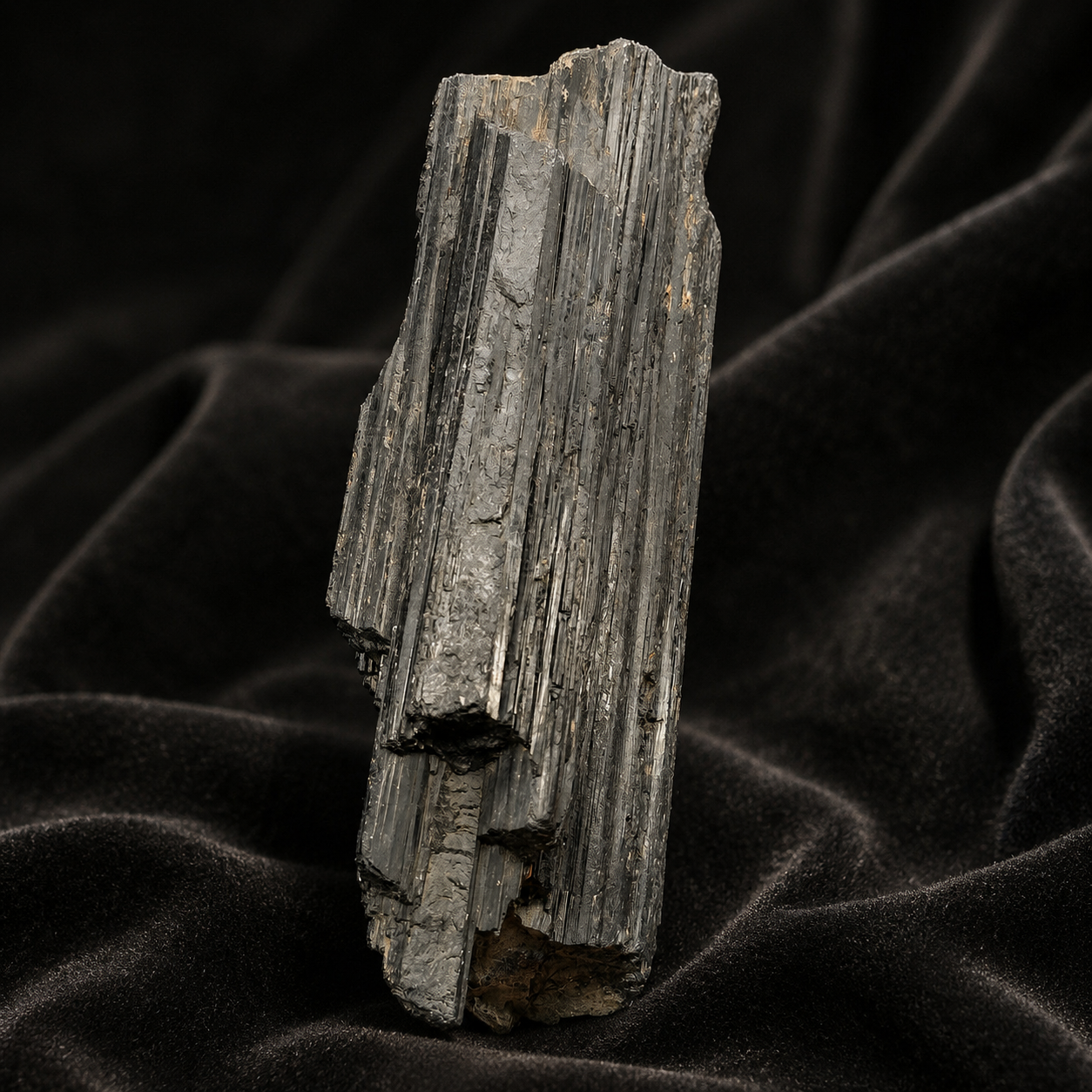 Large rough black tourmaline crystal with vertical banded striations on dark fabric