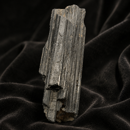 Large rough black tourmaline crystal with vertical banded striations on dark fabric