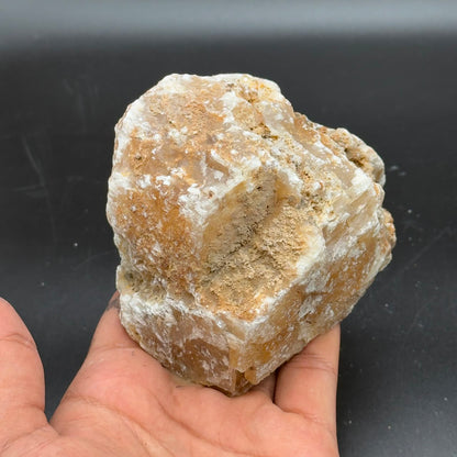 Large rough golden calcite crystal held in hand against dark background