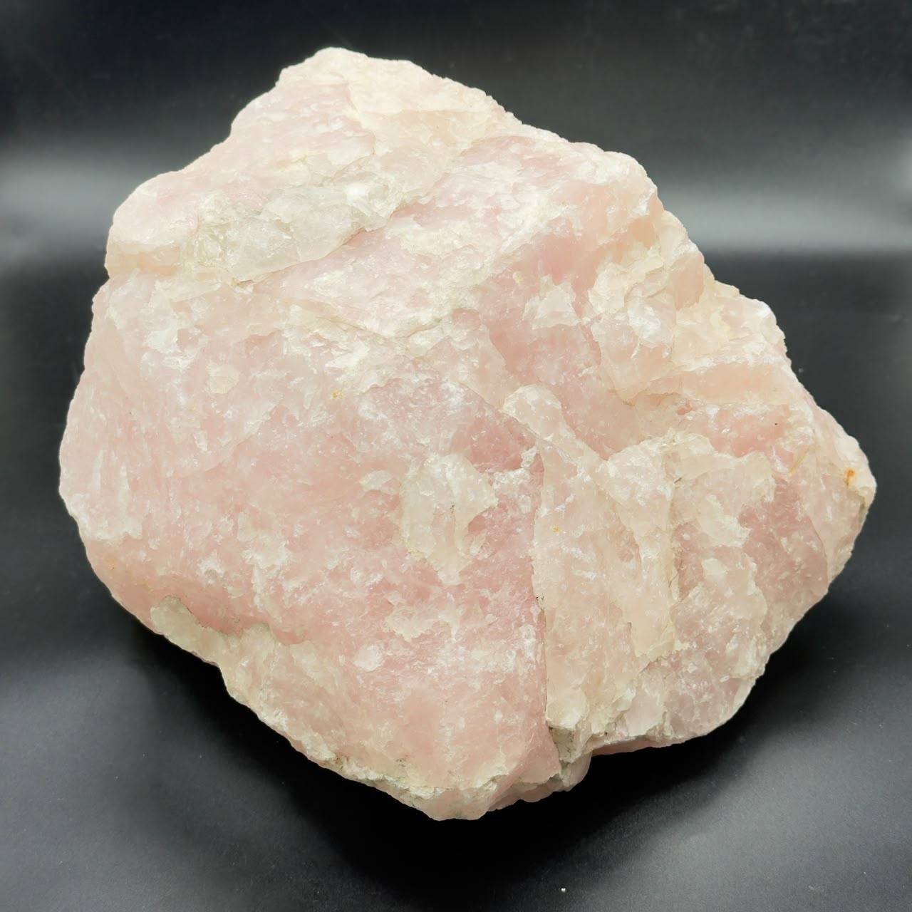 Large rough rose quartz crystal with pink and white crystal texture on dark surface