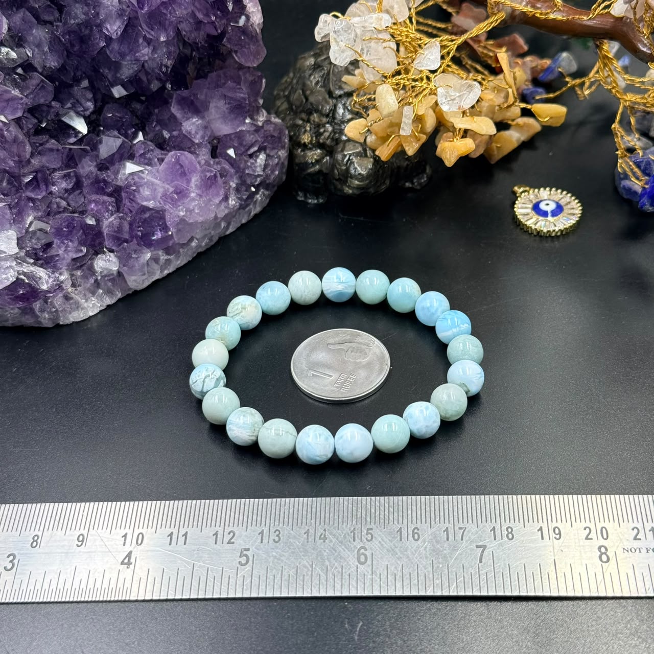 Larimar bracelet with round light blue beads arranged on dark surface and ruler measuring size