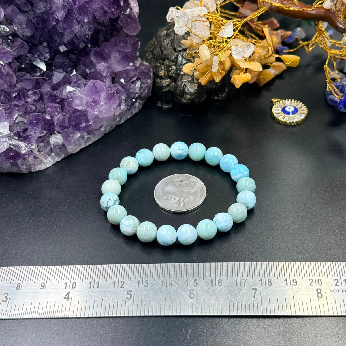 Larimar bracelet with round light blue beads arranged on dark surface and ruler measuring size