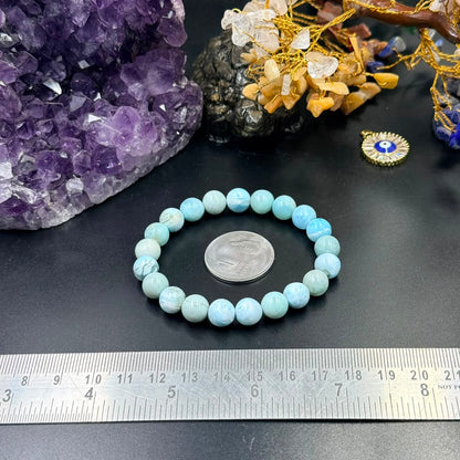 Larimar bracelet with round light blue beads arranged on dark surface and ruler measuring size