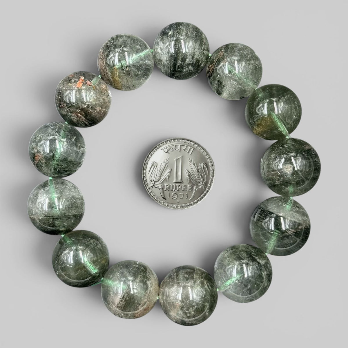 Round translucent Lodolite Garden Quartz beads bracelet with a one rupee coin for scale on gray background