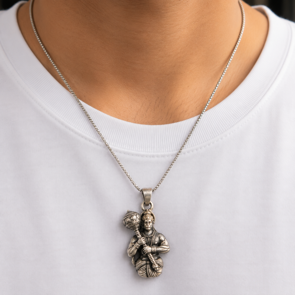 Lord Hanuman gada silver pendant worn on a thin chain against a white shirt