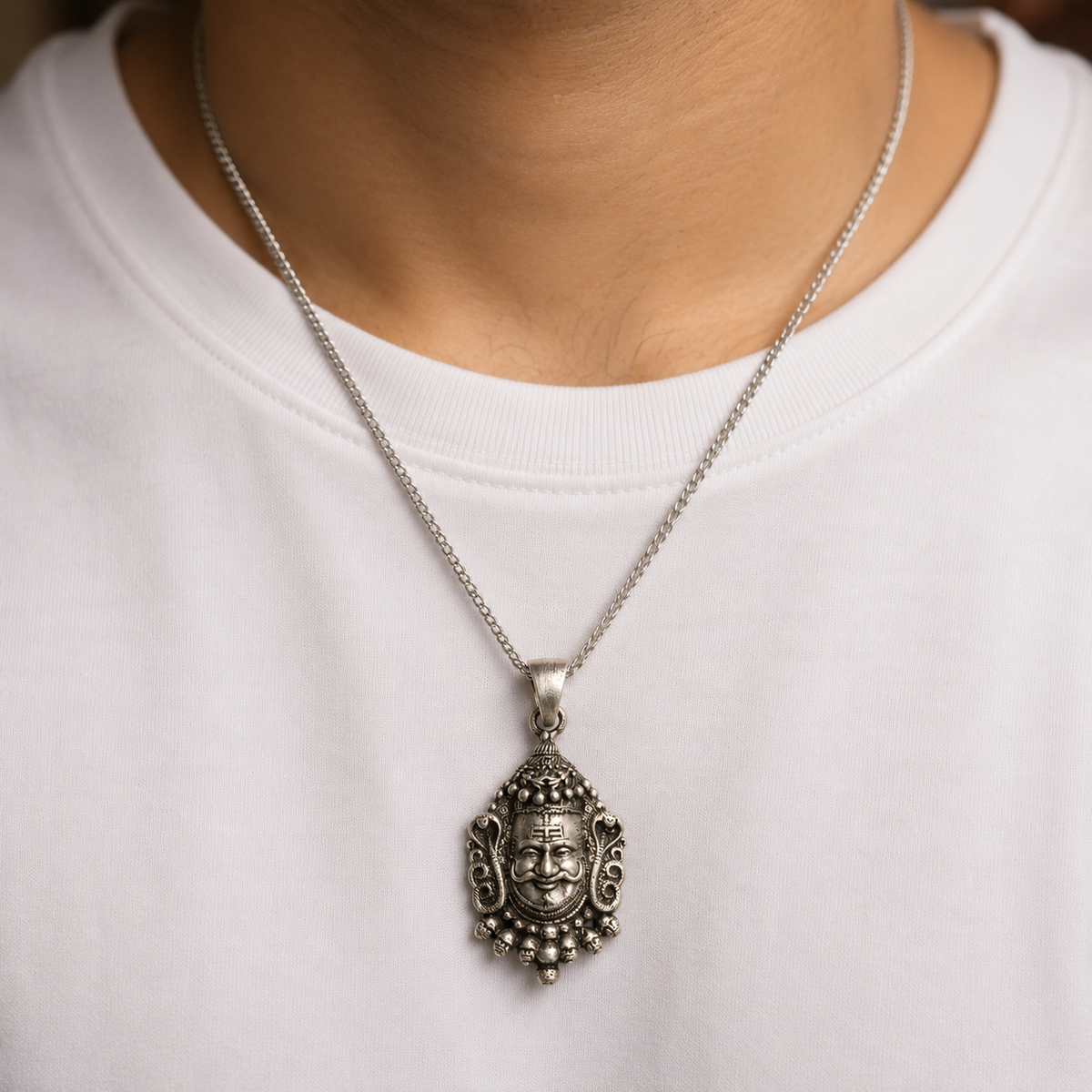 Lord Kuber face pendant on a silver chain worn on a white shirt