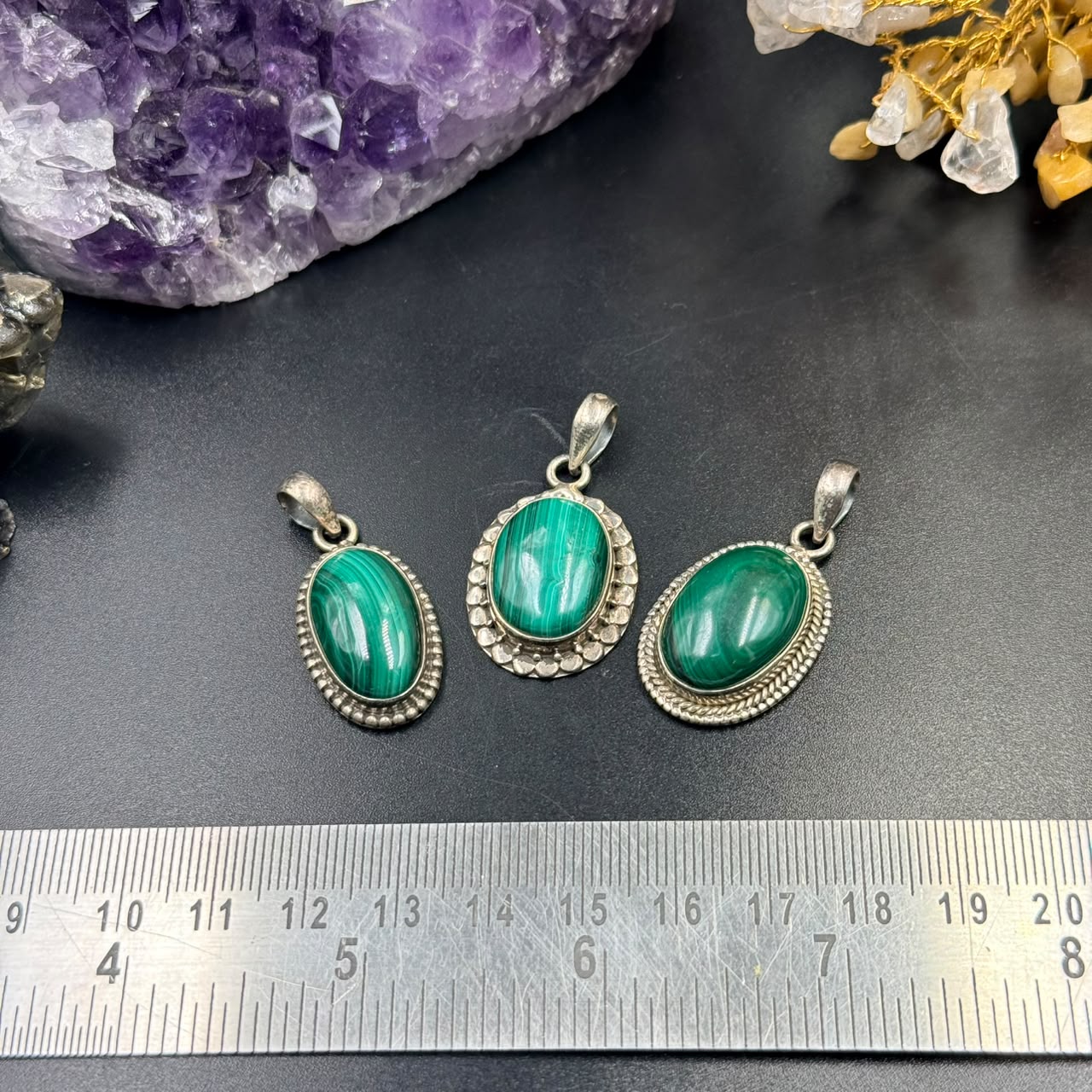 Three malachite green oval silver locket pendants with textured frames shown on dark background