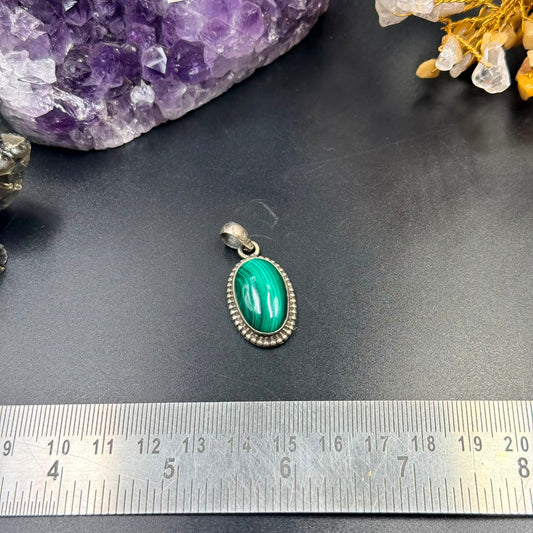 Oval malachite green stone silver locket pendant on black background with ruler for scale