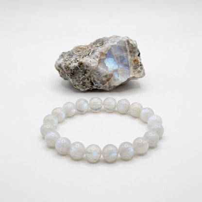 Moonstone bracelet with round beads and a natural moonstone rock specimen on white background
