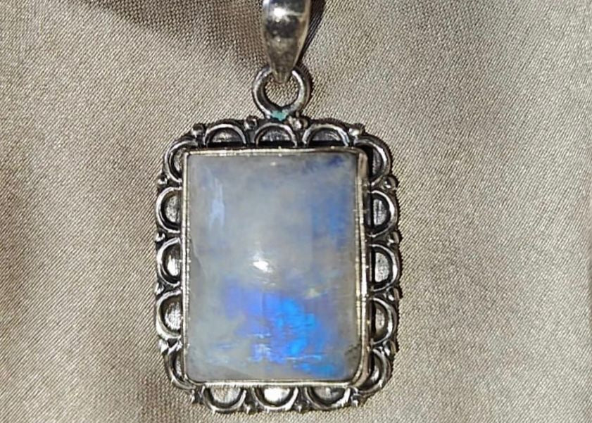 Silver pendant with a rectangular gemstone on a beige fabric background