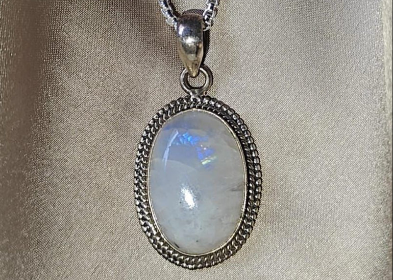 Necklace with a pendant featuring a moonstone on a beige fabric background