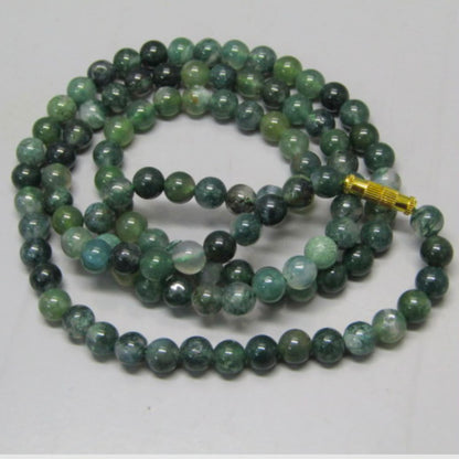 Close-up of moss agate mala bracelet-style strand with gold-toned clasp on white background