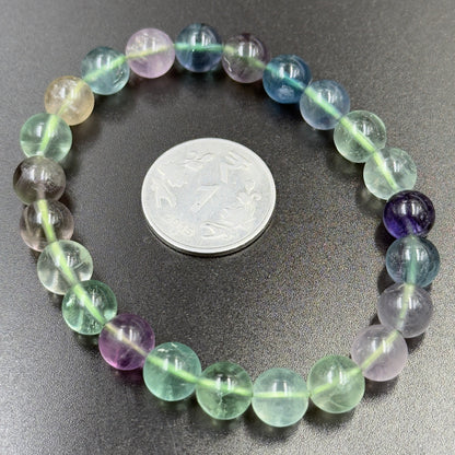 Close-up of multi fluorite bracelet beads with coin for size on dark surface