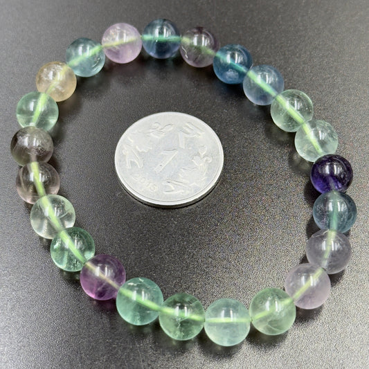 Close-up of multi fluorite bracelet beads with coin for size on dark surface