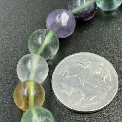 Close-up of multi fluorite bracelet beads next to coin for size on dark surface