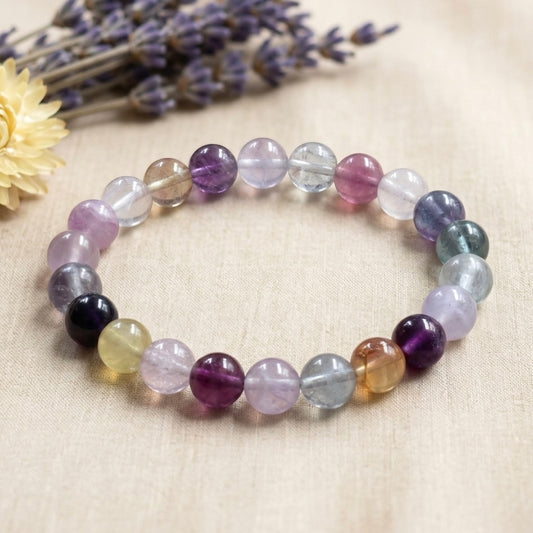 Multi fluorite bracelet with lavender, clear, and green round beads on beige fabric