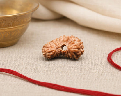 Natural 21 Mukhi rudraksha bead with hollow center on red thread and textured fabric background