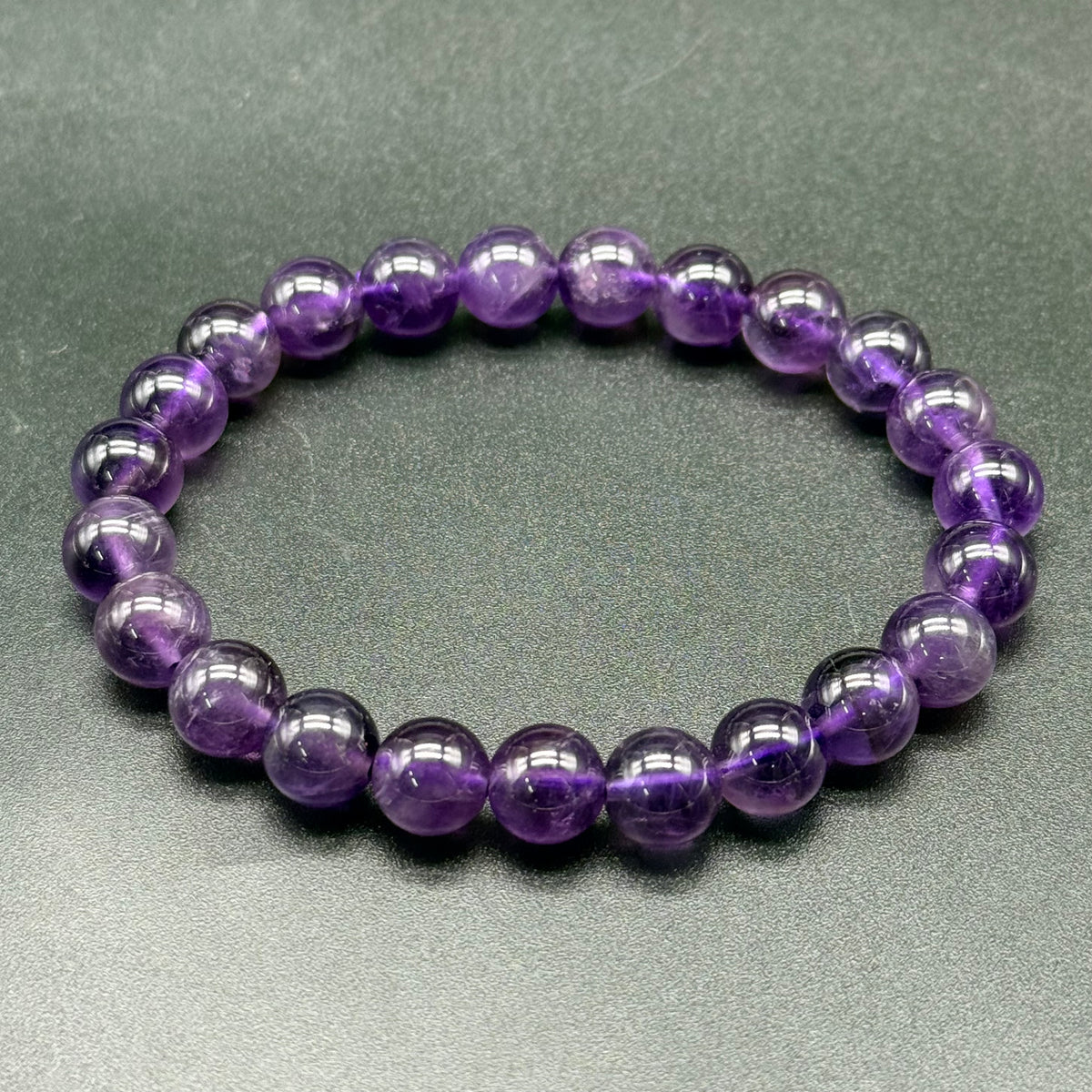 Natural Amethyst Bracelet with polished round beads arranged in a circular pattern on a dark surface