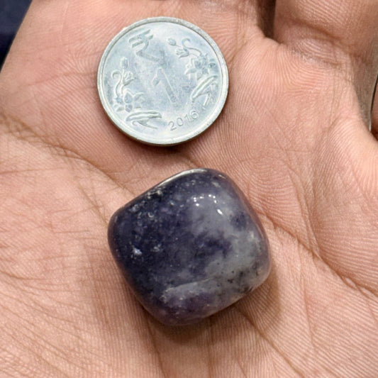 Natural amethyst tumble stone close-up resting in an adult fingertip