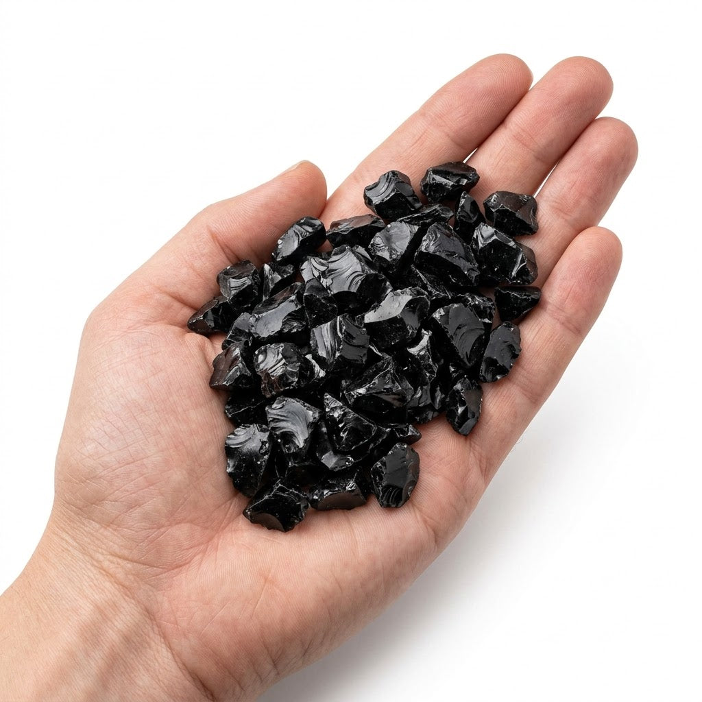 A hand holding a heap of natural raw black obsidian chips on a white background