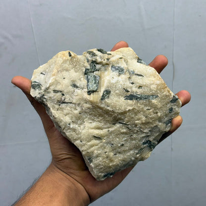 Natural black rutile gemstone rough crystal specimen in hand against gray background