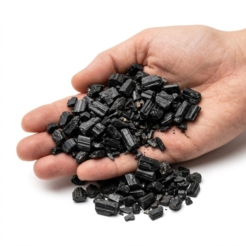 A hand holding a heap of small natural raw black tourmaline chips on a white background