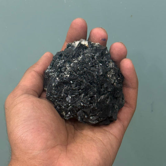 Natural black tourmaline rough crystal with sparkling highlights held in a hand