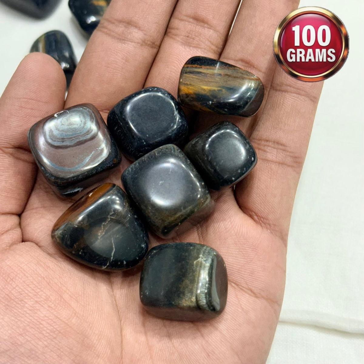 Natural blue tiger eye tumble stones in hand, polished oval shapes with golden bands