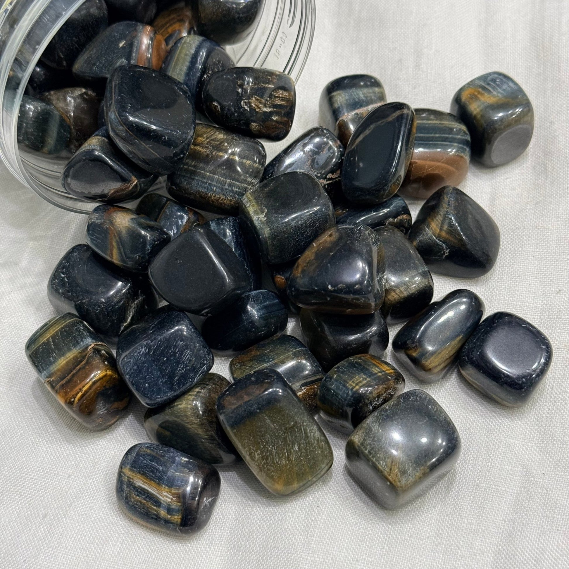 Natural blue tiger eye tumble stones in a clear container, polished with gold streaks