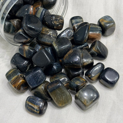 Natural blue tiger eye tumble stones in a clear container, polished with gold streaks