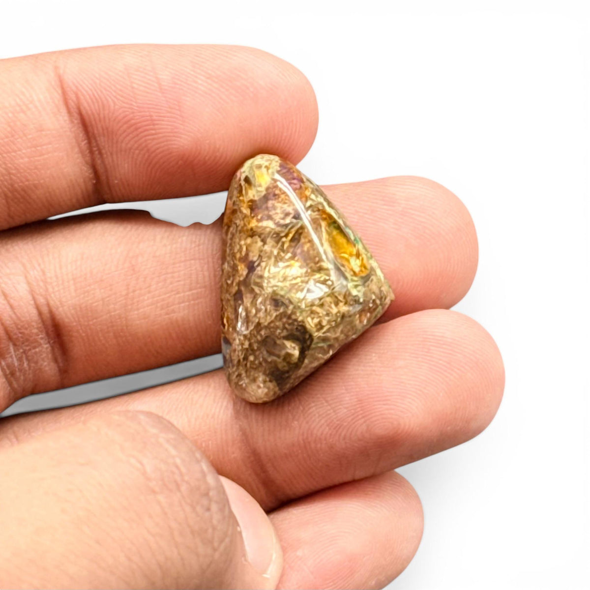 Natural boulder fire opal loose gemstone held in fingers, showing golden glow