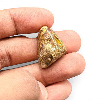 Natural boulder fire opal loose gemstone held in fingers, showing golden glow