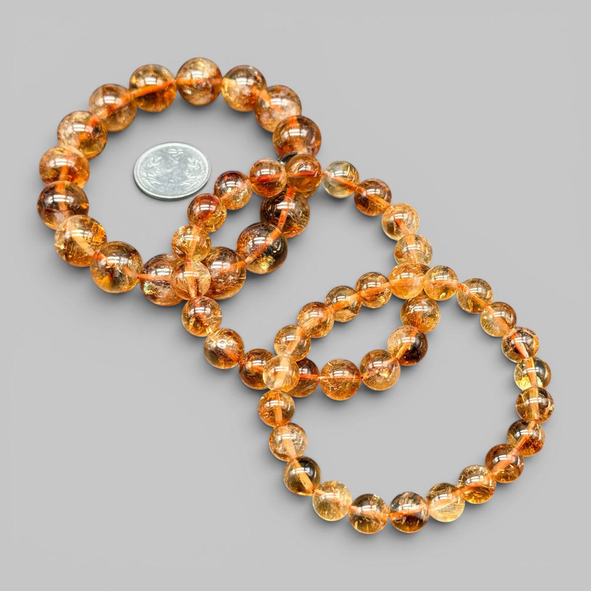 Natural citrine AAA bracelet with round golden beads and coin for scale on gray background
