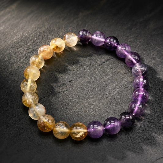 Natural citrine and amethyst bead bracelet with golden and purple round stones on dark surface