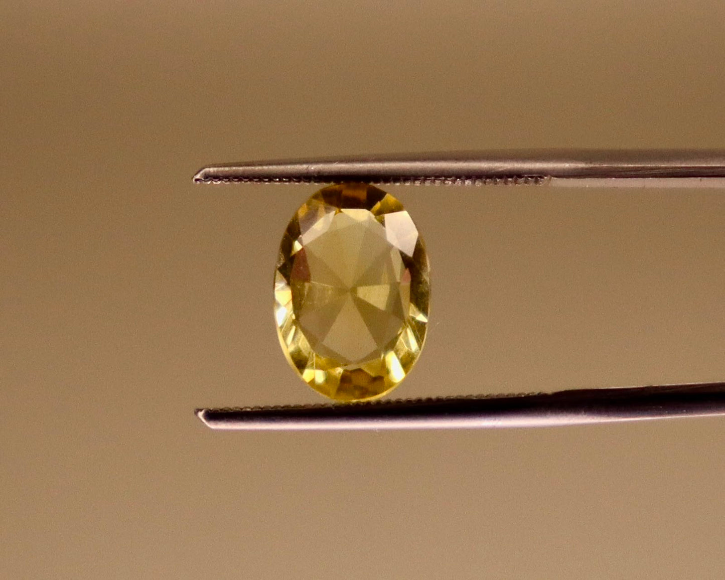 Natural citrine gemstone, oval mixed cut, viewed close-up on tweezers