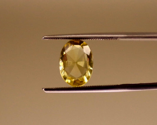 Natural citrine gemstone, oval mixed cut, viewed close-up on tweezers