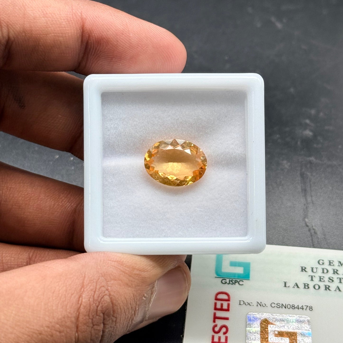 Natural citrine oval mixed cut gemstone in a plastic holder held by hand