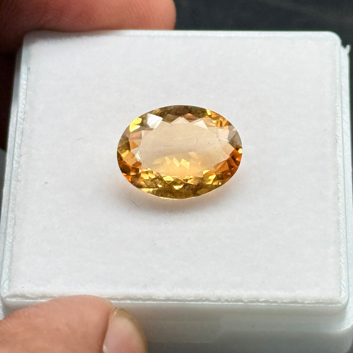 Natural citrine oval mixed cut gemstone viewed from side in a plastic holder
