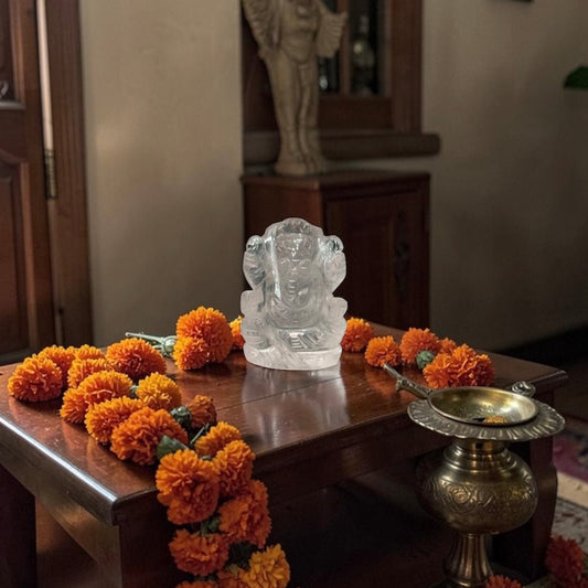 Natural crystal quartz Ganesh Ji carving figure on a wooden table with flowers and oil lamp