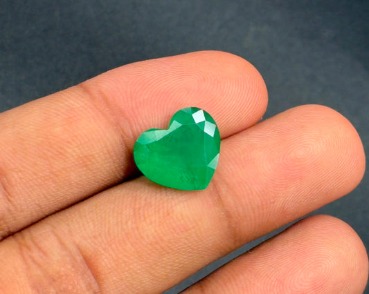 Natural emerald heart mixed-cut gemstone on fingertip close-up