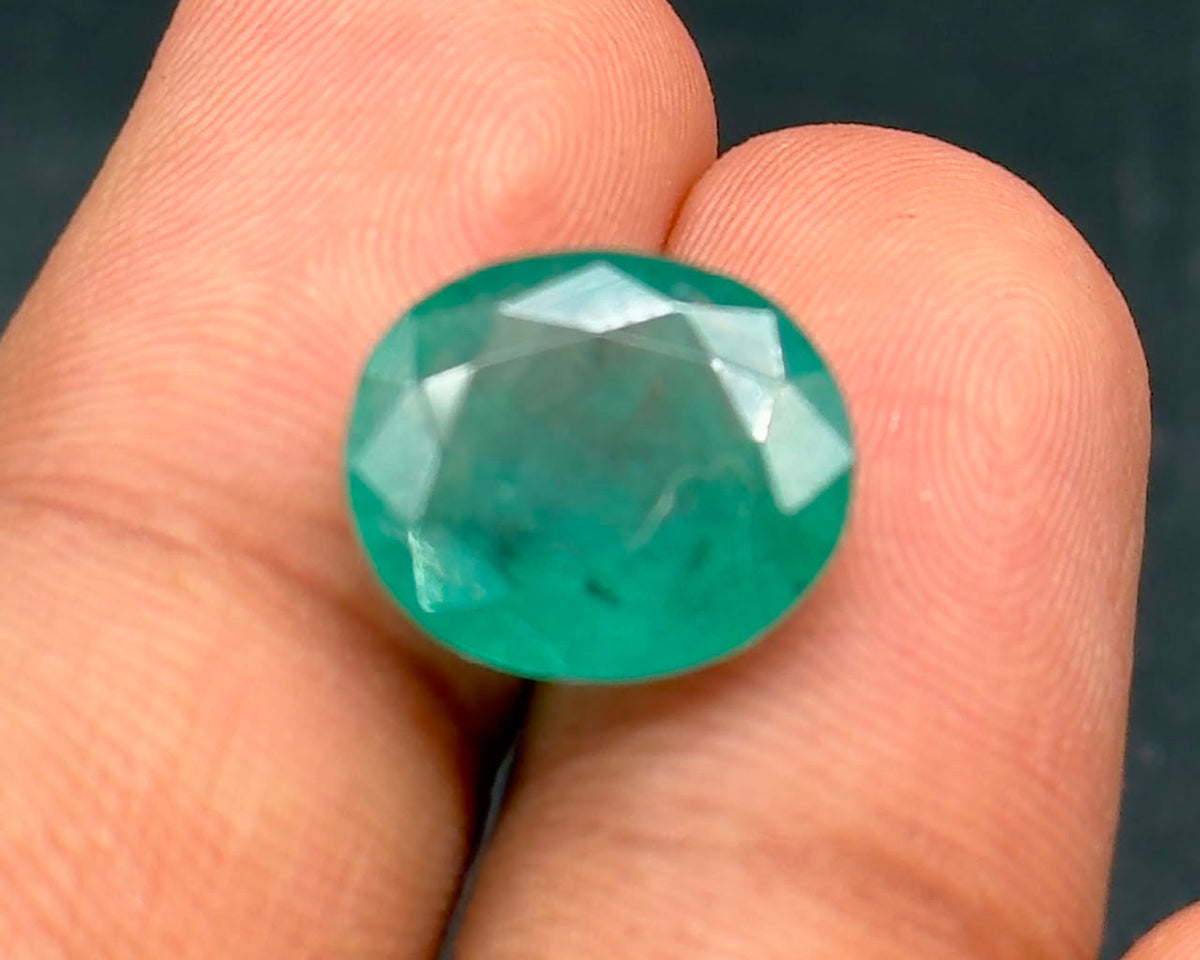 Natural emerald oval gemstone close-up held between fingers, showing green facets