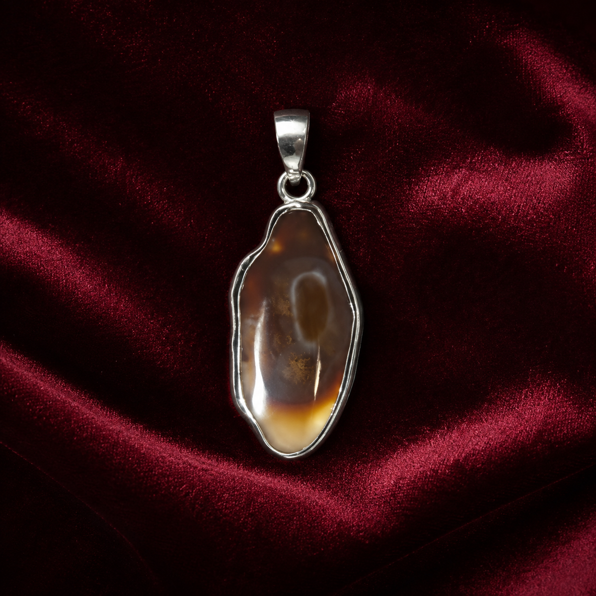 Natural fire agate oval pendant set in 925 silver on a dark red velvet background