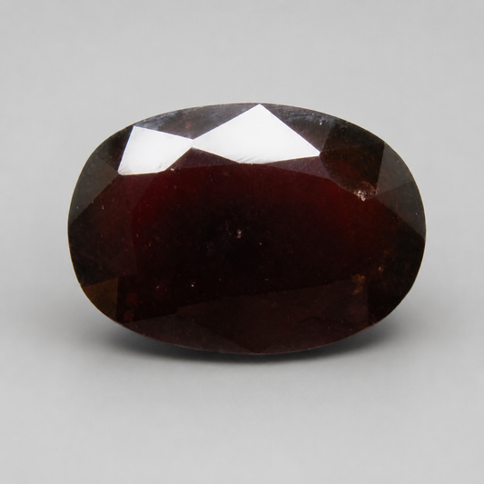 Natural gomedh oval mixed cut gemstone in deep brown maroon color close-up on light background