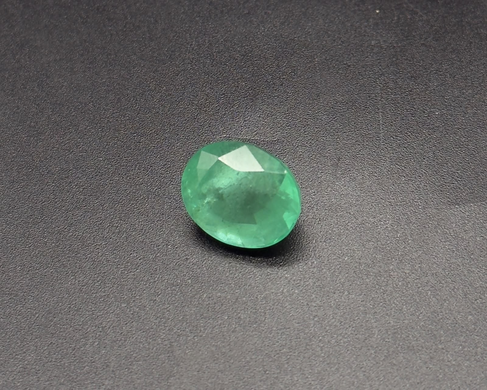 Natural green oval emerald gemstone with faceted sparkle on a dark textured surface