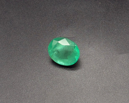 Natural green oval emerald gemstone with faceted sparkle on a dark textured surface