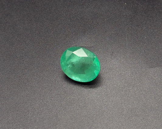 Natural green oval emerald gemstone with faceted sparkle on a dark textured surface